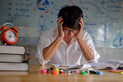 Young man studying with school supplies on table at home