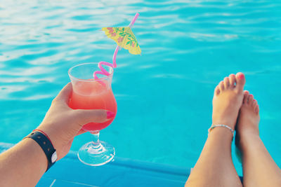 Midsection of woman holding drink in swimming pool
