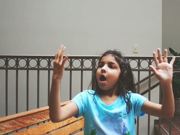 Girl with open mouth while gesturing against railing at home