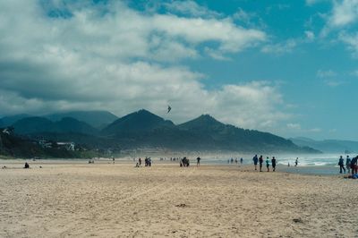 People at cannon beach against cloudy sky