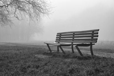 Empty bench on field during foggy weather