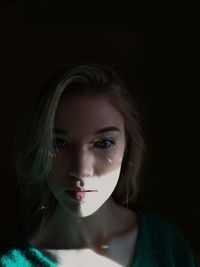 Close-up portrait of beautiful young woman against black background