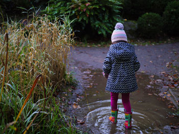 Rear view of young girl walking in the muddy puddle 