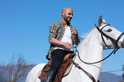Smiling man sitting on horse against sky