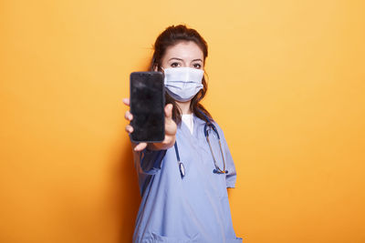 Young woman using mobile phone while standing against yellow background