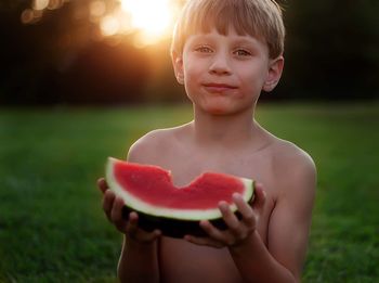 Portrait of shirtless boy eating watermelon during sunset