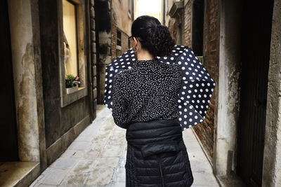 Rear view of woman with umbrella walking on narrow footpath in city