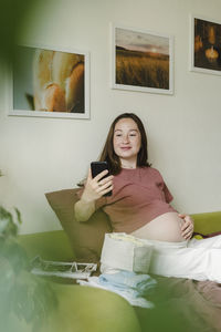 Smiling pregnant woman using mobile phone at home