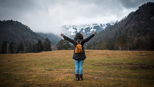 Full length rear view of woman with arms raised looking at mountains during winter