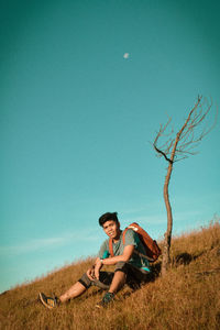 Young man sitting on field against clear sky