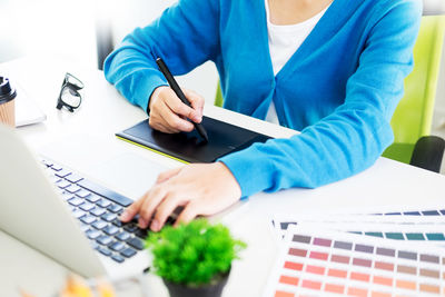 Midsection of design professional using graphics tablet and laptop on desk