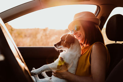 Side view of woman with dog sitting at car