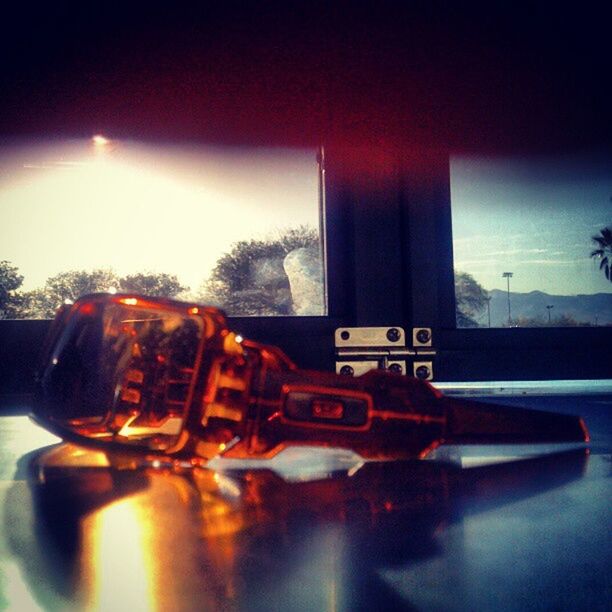 indoors, close-up, glass - material, still life, selective focus, no people, focus on foreground, reflection, table, metal, sunlight, auto post production filter, red, bottle, transparent, window, sky, lens flare, day, single object