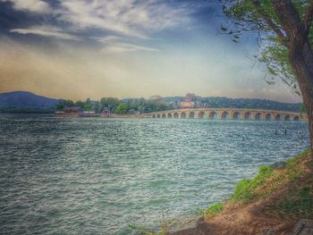 Bridge over river against cloudy sky