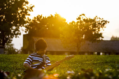 Boy playing guitar on field during sunset