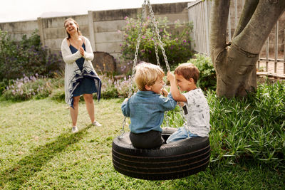 Smiling mother standing while kids playing on swing