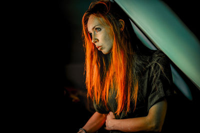 Portrait of young woman standing against black background