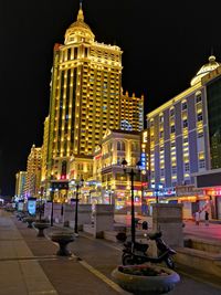 Illuminated building by road against sky at night