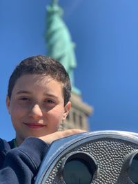 Low angle portrait of boy standing against statue in city