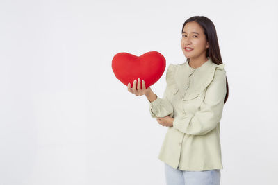 Smiling young woman holding heart shape over white background