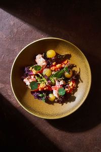 Top view of bowl with delicious crab salad with fresh vegetables and herbs placed on brown table