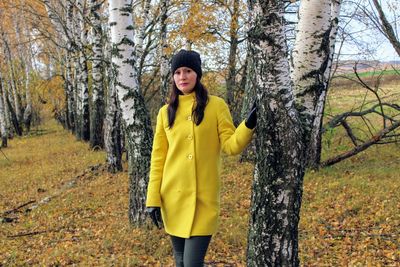 Portrait of smiling young woman standing in forest during autumn