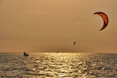 People in sea against sky during sunset