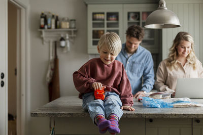 Boy playing in kitchen, parents in background