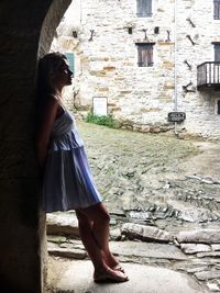 Side view of woman standing against wall of building