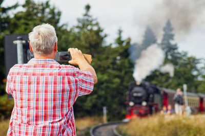 Rear view of man photographing steam train