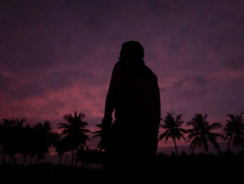 Silhouette man standing by palm trees against sky at sunset