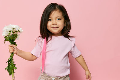 Portrait of young woman standing against pink background