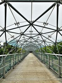 Footbridge in greenhouse against sky