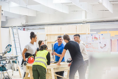 Male instructor teaching about level to trainees standing at workbench in illuminated workshop