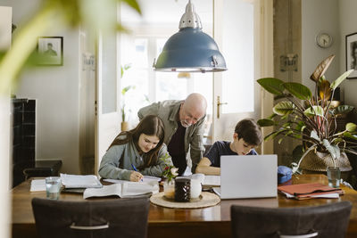 Senior man assisting grandchildren studying at home