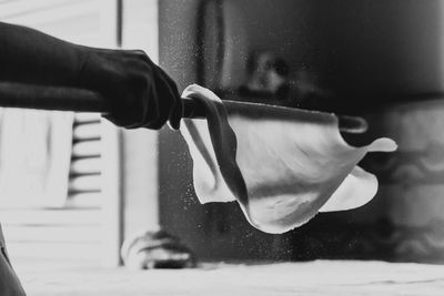 Cropped hand of chef holding dough with stick on table in kitchen