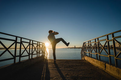 Man standing on railing by sea against clear sky