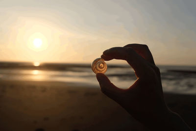 Man holding cigarette at beach against sky during sunset