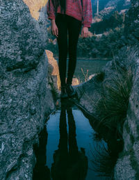 Low section of woman standing by reflection in puddle amidst rock formations