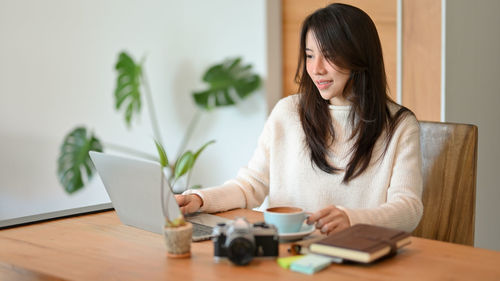 Young woman using phone while sitting on table