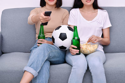 Midsection of young friends watching soccer match on sofa at home