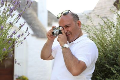 Man photographing with camera while standing against plant