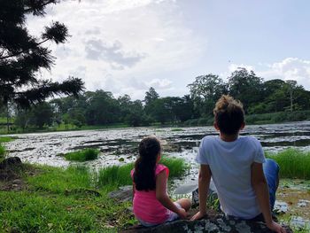 Rear view of women sitting on riverbank against sky