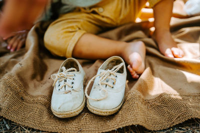 Fabric shoes placed on blanket on background of crop anonymous kid sitting barefoot in nature