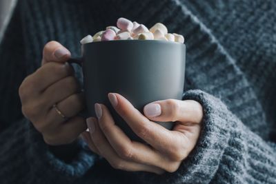 Cropped hands of woman holding marshmallows in mug