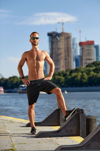 Rear view of shirtless man standing on retaining wall
