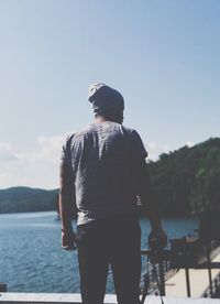 Rear view of man with camera standing against sea