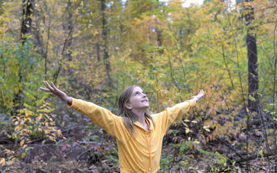 Girl with arms outstretched standing against trees in forest