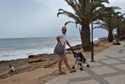 Portrait of man standing with baby stroller on promenade against sky