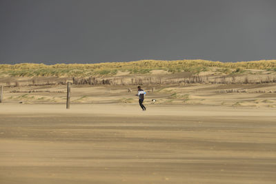 Man running at beach against clear sky
